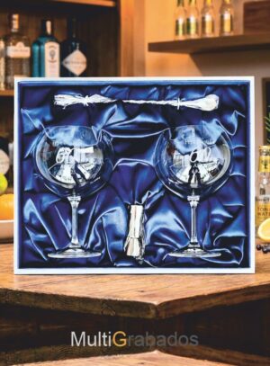 Pack de regalo premium con dos copas de balón para gin tonic grabadas, cuchara de coctelería y medidor metálico en estuche azul con interior de seda.